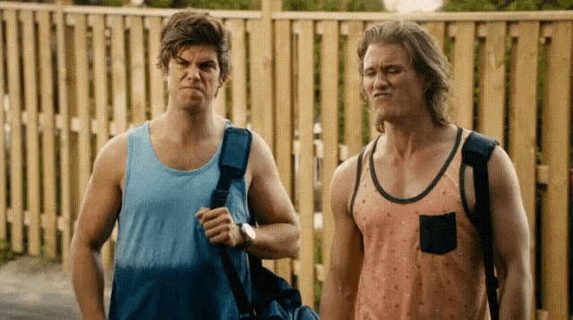 two men standing next to each other in front of a fence