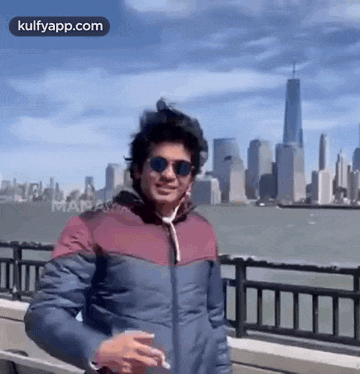 a man in a jacket and sunglasses is standing in front of a city skyline .