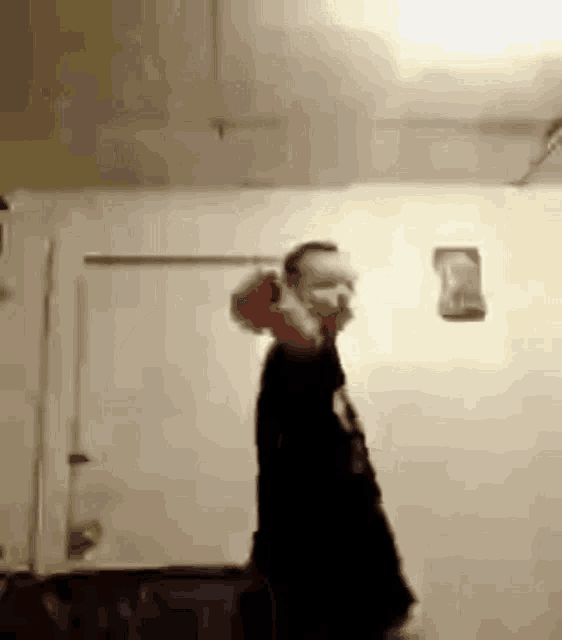 a man in a black shirt is standing in front of a white wall while talking on a phone .