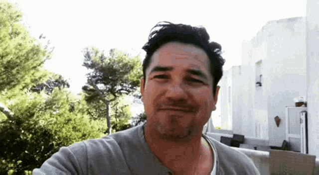 a man with a beard is smiling in front of a white building and trees