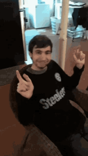 a man wearing a black steelers sweater is giving the ok sign