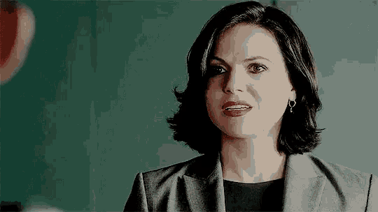 a woman in a suit and earrings is looking at the camera with a serious look on her face .
