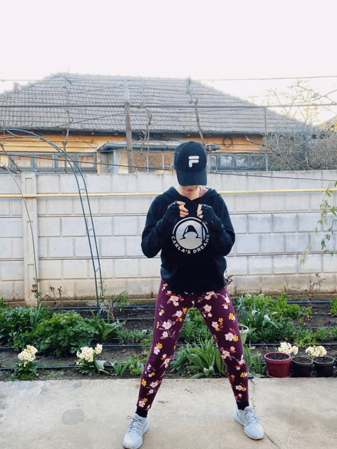 a woman wearing a fila hat stands in front of a brick fence