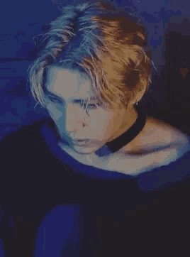 a man with blonde hair and a choker around his neck is looking down .