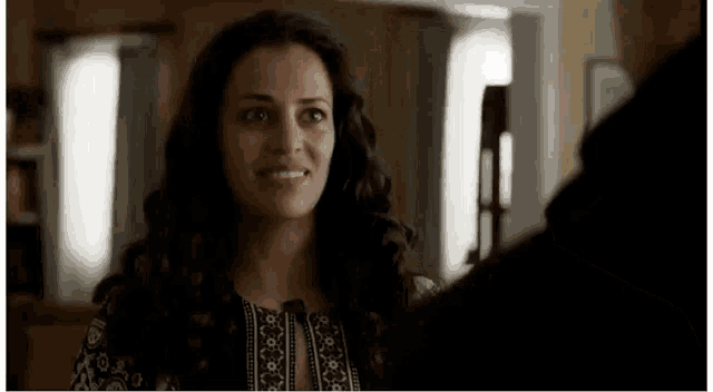 a woman with long hair is smiling and looking at a man in a room .
