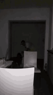 a man in a yellow shirt is standing in a dark room behind a table