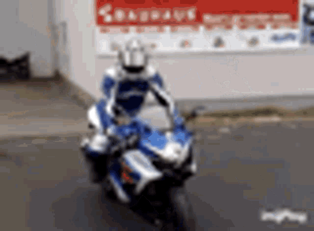 a man is riding a blue and white motorcycle on a street in front of a building .
