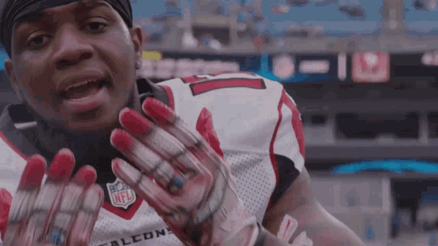 a man wearing a falcons jersey holds his hands up