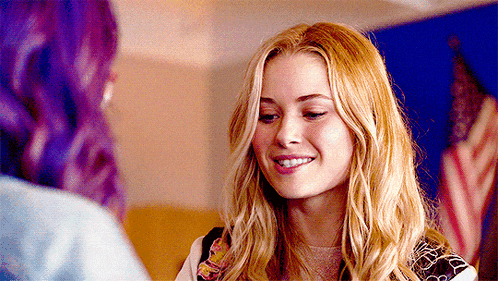 a woman with blonde hair and purple hair smiles while talking to another woman