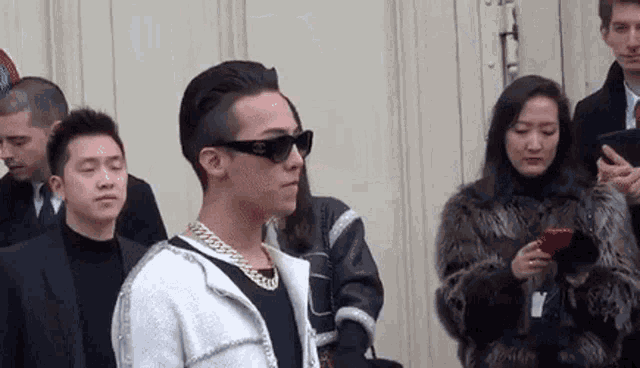 a man wearing sunglasses and a necklace is standing in a crowd of people .
