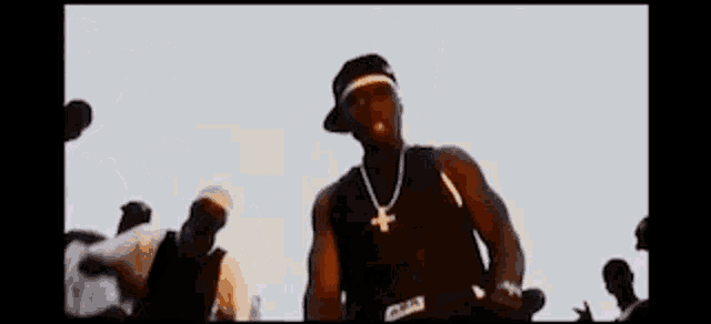 a man wearing a hat and a necklace with a k on it is standing in front of a crowd .