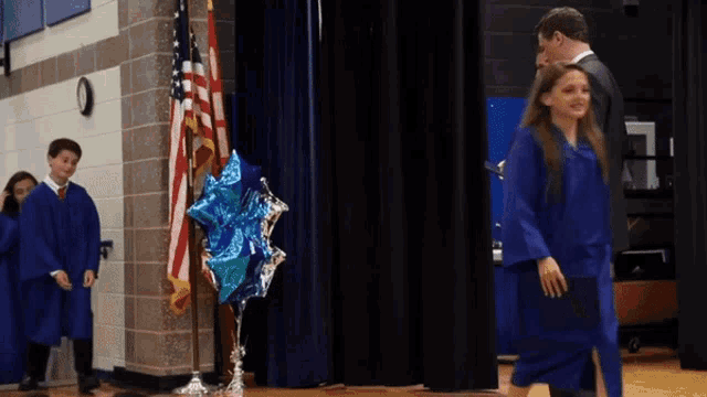 a girl in a blue graduation gown walks down the stage