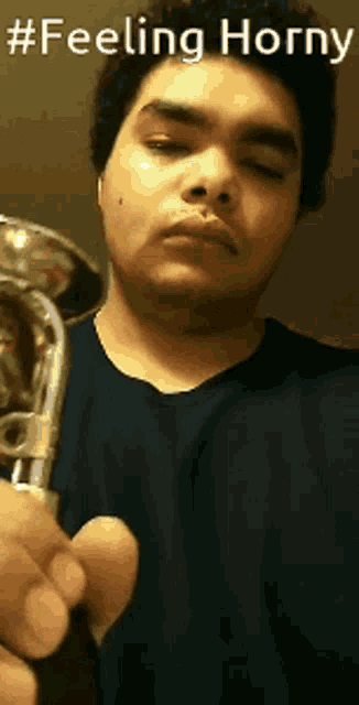 a man in a blue shirt is holding a trombone with the words feeling horny above him