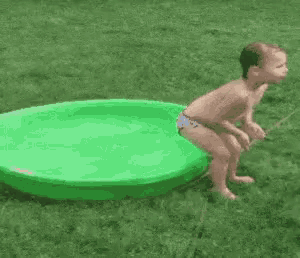 a baby is jumping into a green pool in the grass .