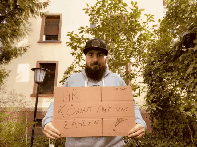 a man with a beard is holding a cardboard sign that says " ihr könnt auf uns zahlen "