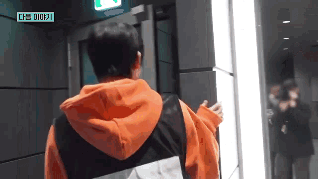 a man in an orange hoodie is standing in front of a door in a dark room .