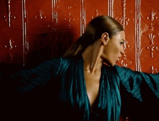 a woman in a blue robe is standing in front of a red wall with her arms outstretched .