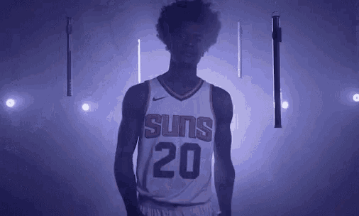 a basketball player is standing in a dark room wearing a suns jersey .