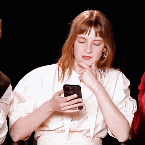 a woman in a white shirt is holding a black cell phone