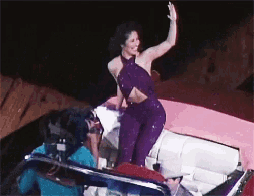 a woman in a purple outfit is standing on a boat waving
