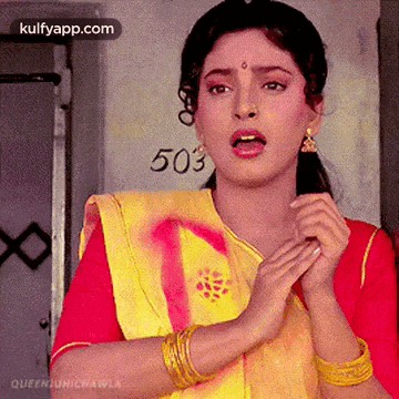 a woman in a yellow and red saree is standing in front of a door with the number 503 written on it .