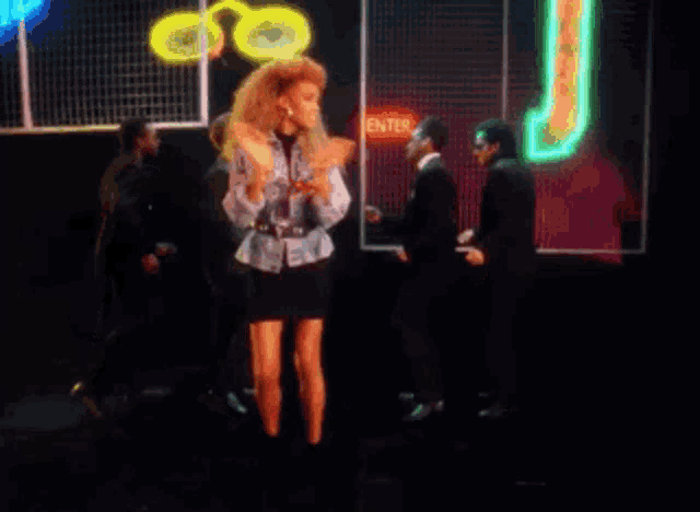a group of people are dancing in front of a neon sign that says j.