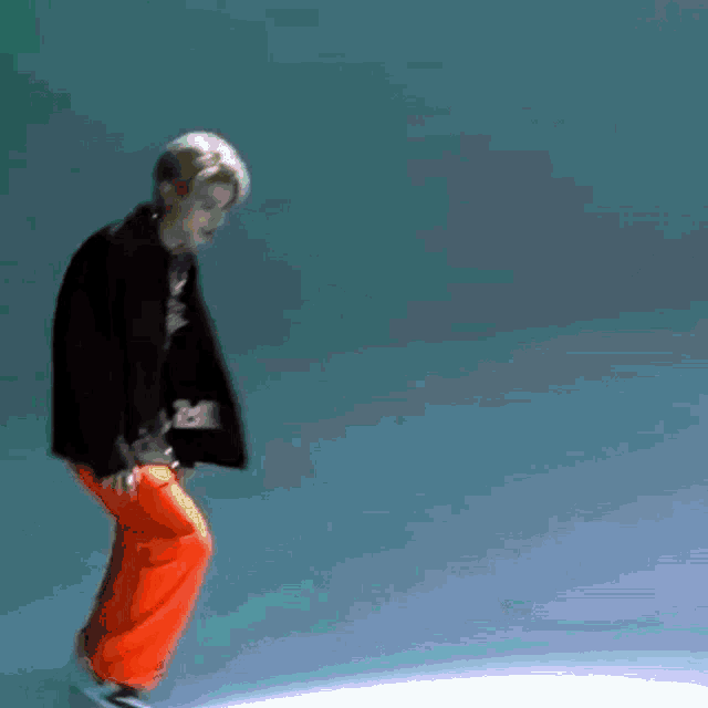 a man in a black jacket and orange pants is dancing in front of a blue background