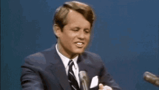 a man in a suit and tie is giving a speech in front of two microphones .