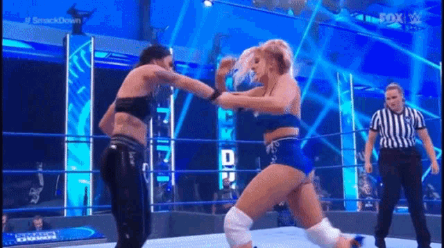 two women are fighting in a wrestling ring while a referee watches .