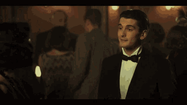 a man in a tuxedo and tie is standing in a crowd of people