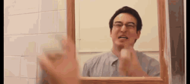 a man with glasses looks at himself in the mirror