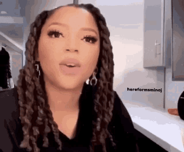 a woman with dreadlocks and hoop earrings is sitting at a table in a kitchen .