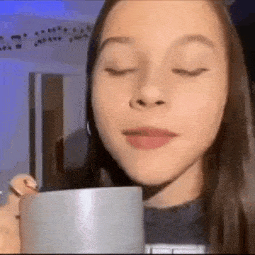 a girl is holding a cup of coffee in her hand and drinking from it .
