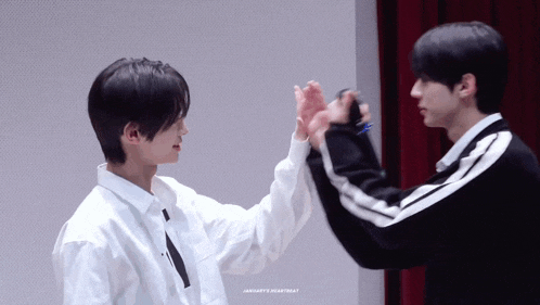 two boys are giving each other a high five while standing next to each other .