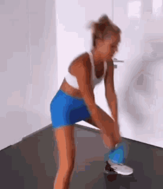 a woman in blue shorts and a white tank top is doing squats on a gym floor .
