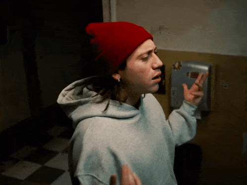 a woman wearing a red beanie and a grey hoodie is making a peace sign