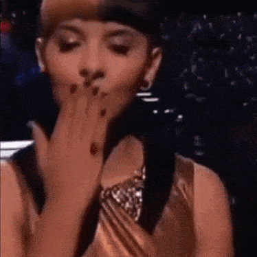 a woman in a gold dress is covering her mouth with her hand .