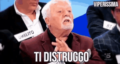 a man with a beard and a name tag that says umberto is sitting in front of a group of men .