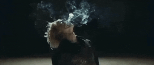 a woman is smoking a cigarette in a dark room and smoke is coming out of her mouth .
