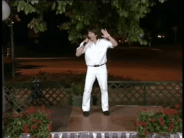 a man in a white shirt and white pants is singing into a microphone .