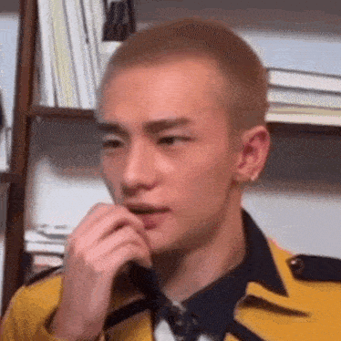 a young man with a shaved head is wearing a yellow jacket and tie and holding his hand to his mouth .