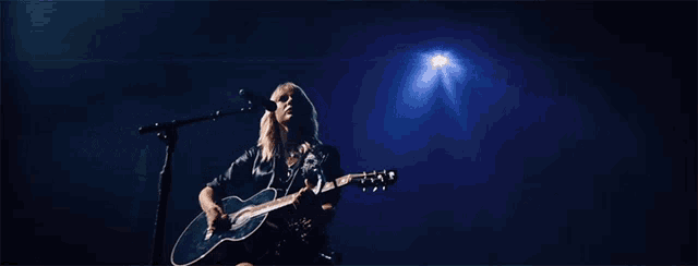 a woman is singing into a microphone while playing an acoustic guitar