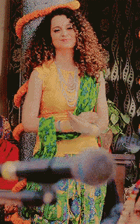 a woman with curly hair wearing a yellow top and green pants