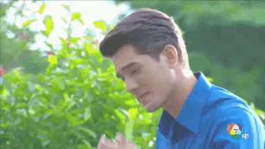 a man in a blue shirt is standing in front of a bush with the number 7 on his sleeve .