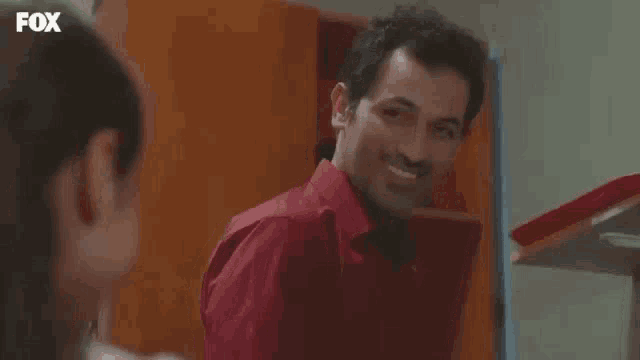 a man in a red shirt is smiling while looking at a woman .