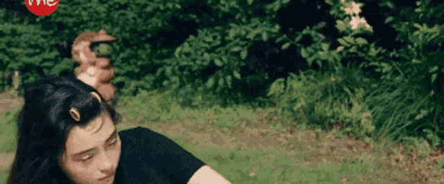 a woman in a black shirt is sitting in the grass with her hair in a ponytail .