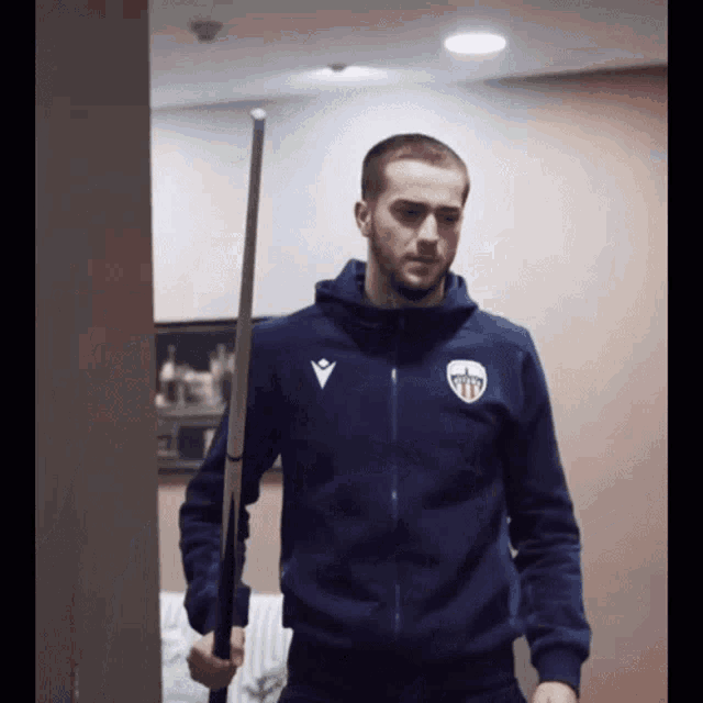 a man in a blue jacket holds a pool cue in his right hand