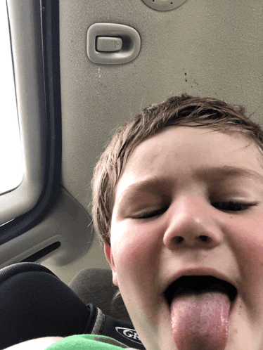 a young boy sticking his tongue out while sitting in a car seat