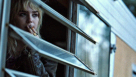 a woman is smoking a cigarette and looking out a window .