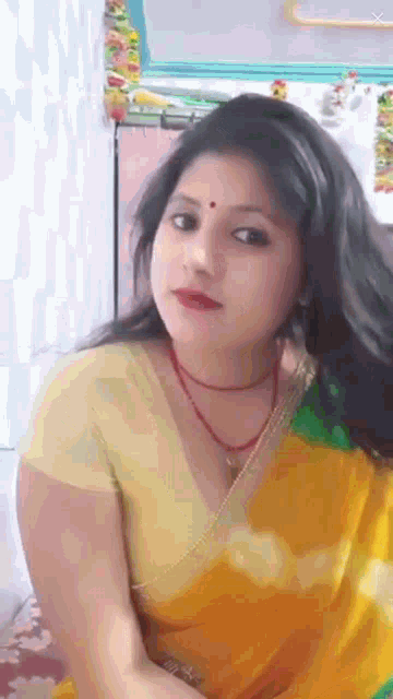 a woman wearing a yellow blouse and a red necklace looks at the camera
